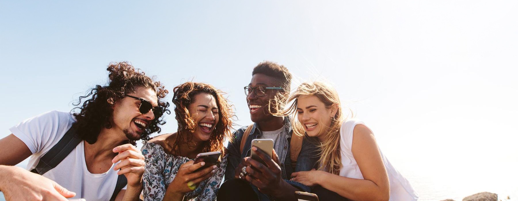 a group of friends sit outside laughing over their cell phones